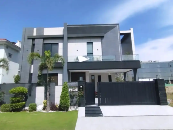 Front exterior view of 1 Kanal modern luxury house with palm trees green lawn and grey facade in Lake City M3 Lahore