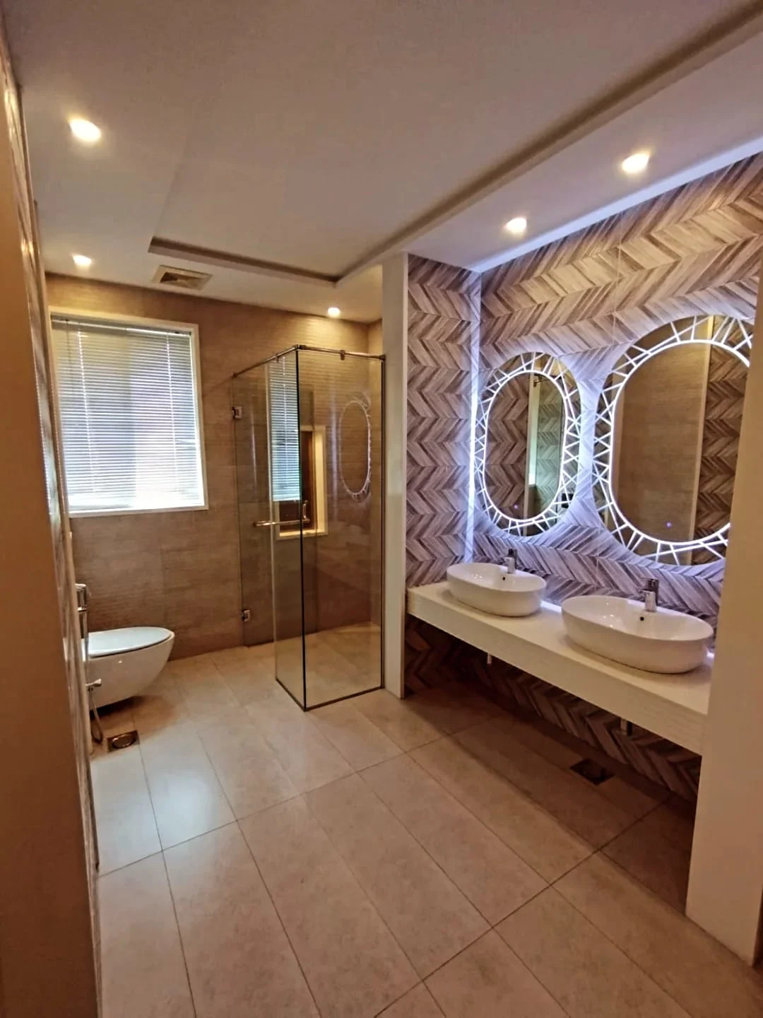 Modern Master Bathroom – 1 Kanal Luxury House Block M2 Lake City Lahore Luxury master bathroom with dual vessel sinks, LED oval mirrors, herringbone wall tiles and glass shower cabin in Lake City Lahore house