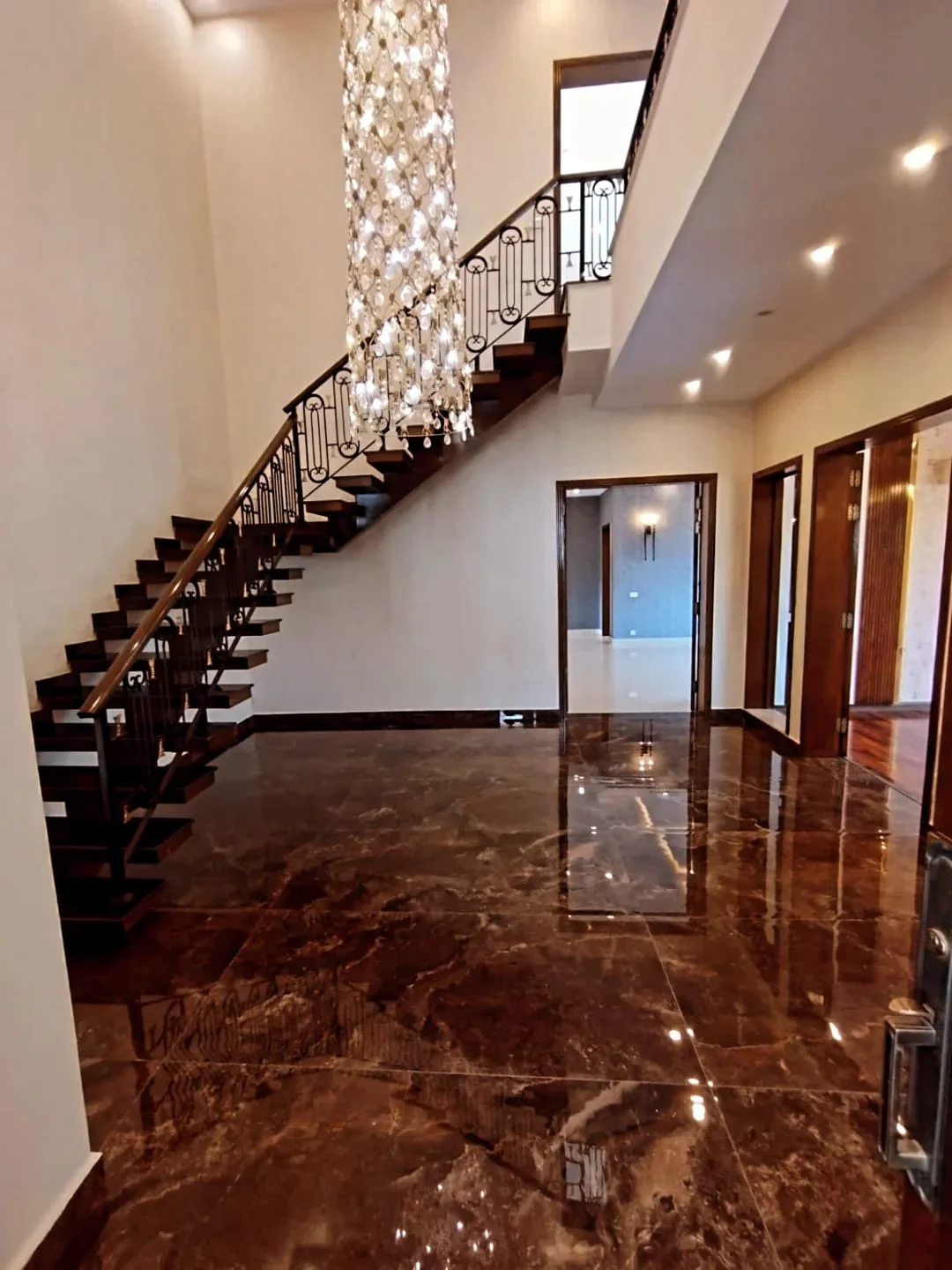 Stunning Staircase & Entrance Foyer – 1 Kanal Luxury House Lake City Lahore Double height entrance foyer with dark marble flooring, wooden floating staircase and crystal pendant chandelier in 1 Kanal house Lake City