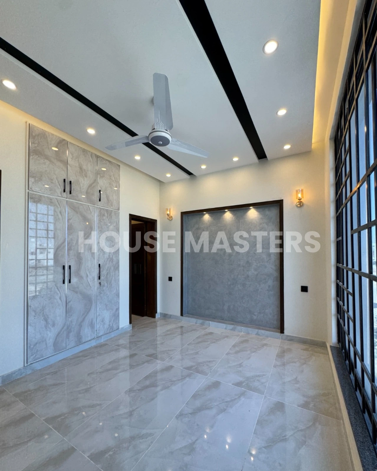 Luxury 5 Marla house living room with large black-framed windows, ceiling fan, and ambient lighting in Bahria Orchard, Lahore.