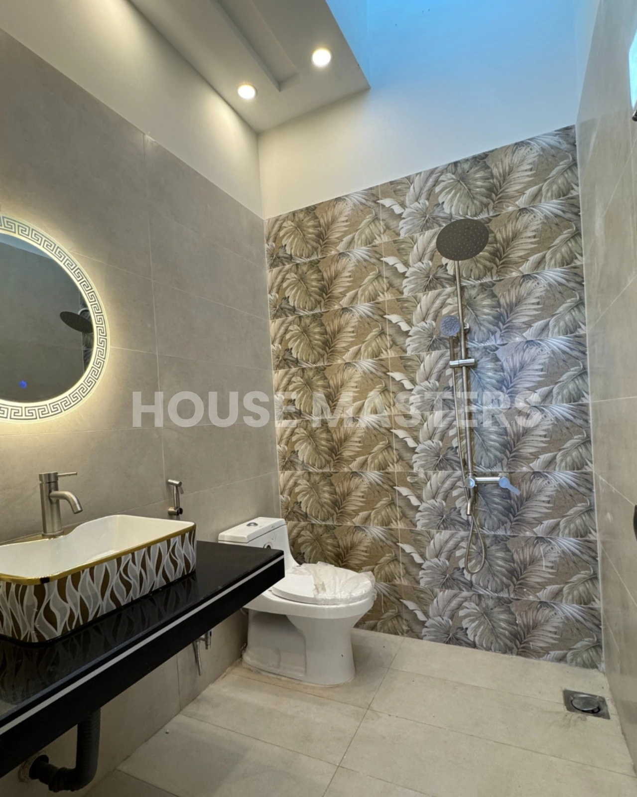Stylish bathroom with leaf-pattern accent wall, black countertop, and illuminated round mirror in 5 Marla luxury home, Bahria Orchard.