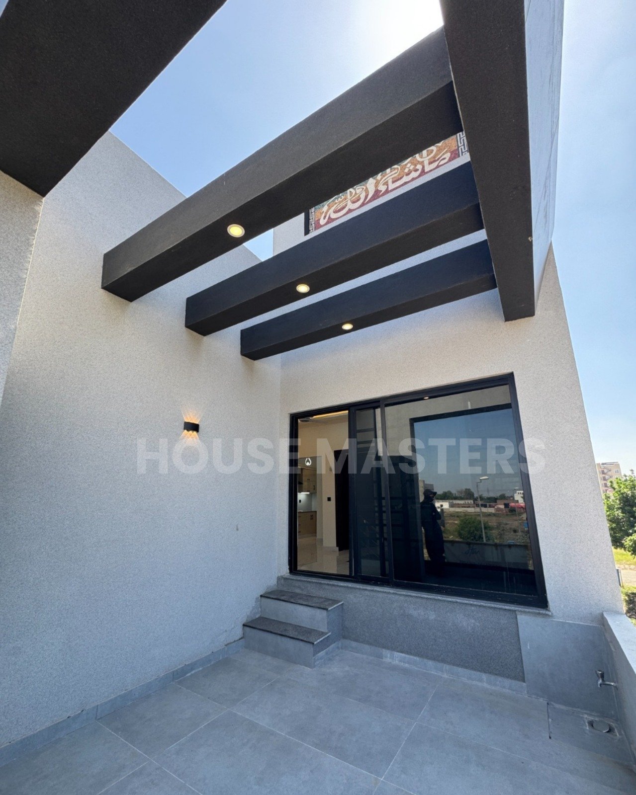 Modern balcony with black beams, grey flooring, and partial outdoor view in 5 Marla premium home, Bahria Orchard.