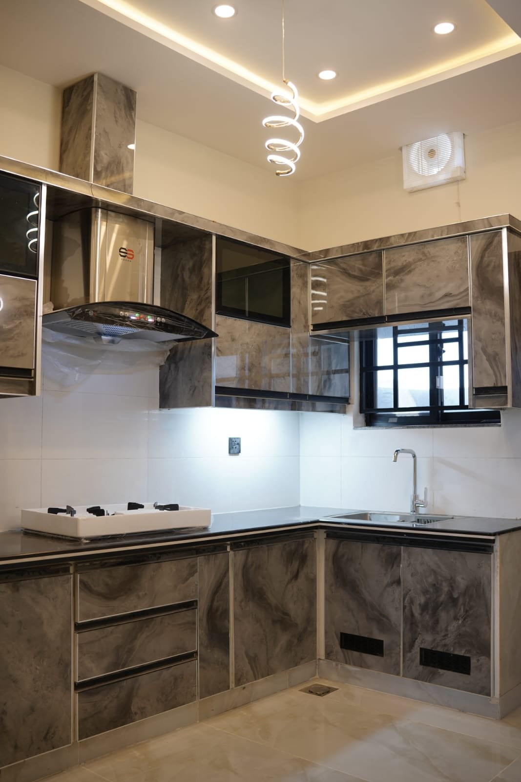 Contemporary kitchen with beige cabinets, black countertops, and integrated appliances in premium 5 Marla residence, Bahria Orchard.