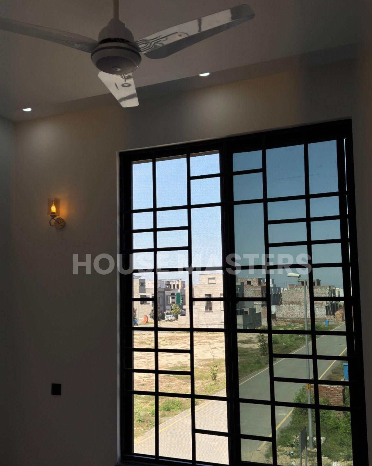 Luxury 5 Marla house living room with large black-framed windows, ceiling fan, and ambient lighting in Bahria Orchard, Lahore.
