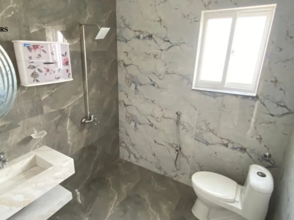 Modern bathroom with premium marble tiles, floating vanity, and round mirror in Lake City Lahore M8 house.