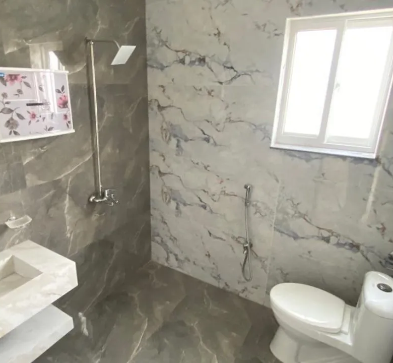 Modern bathroom with premium marble tiles, floating vanity, and round mirror in Lake City Lahore M8 house.